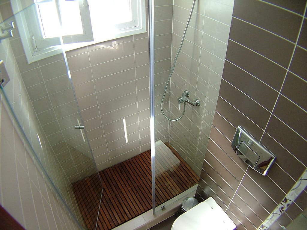 Reforma de baño con ducha de obra y tarima de madera con mampara sin perfiles