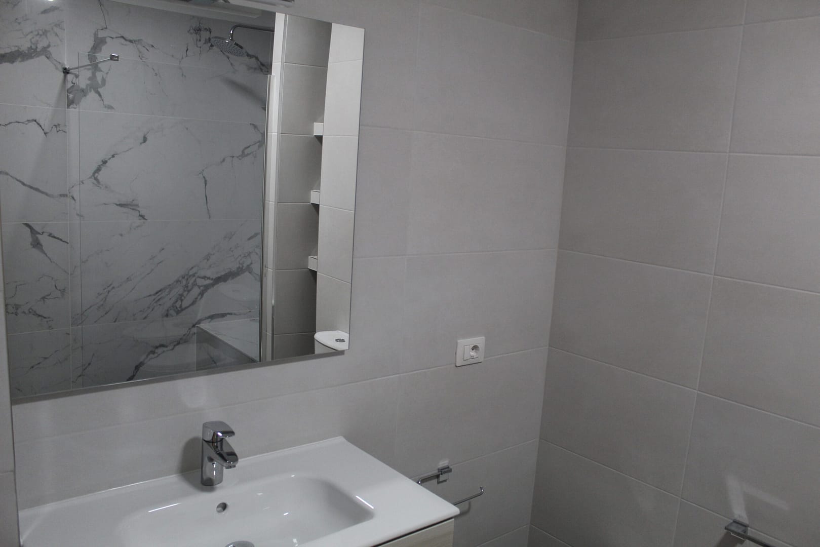 Reforma de baño con azulejo gris y zona de ducha con marmol